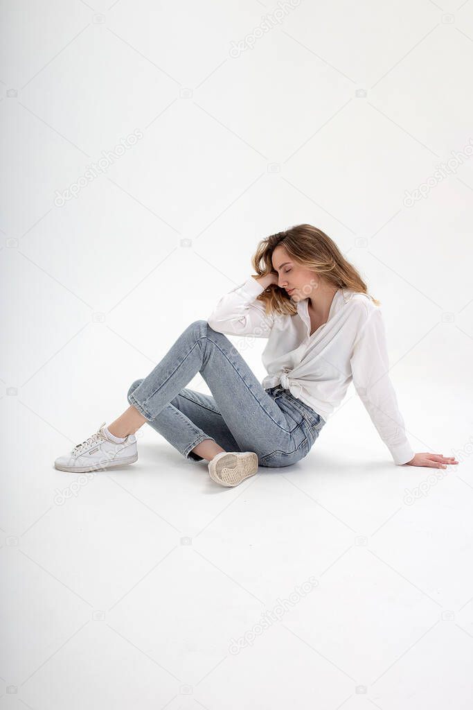 young cute pensive caucasian girl posing in white shirt, blue jeans at studio