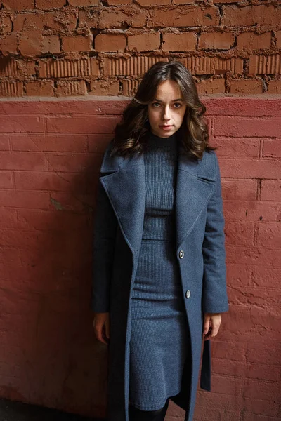 Giovane ragazza premurosa in cappotto grigio e dolcevita posa davanti all'edificio rosso — Foto Stock