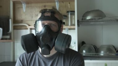 Gaz maskeli adam evde mutfakta oturuyor. Kimyasal silah, virüs koruması