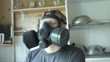 Gaz maskeli adam evde mutfakta oturuyor. Kimyasal silah, virüs koruması
