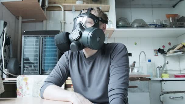 Mand i gasmaske sidder i køkkenet derhjemme. kemisk våben, virusbeskyttelse – Stock-video