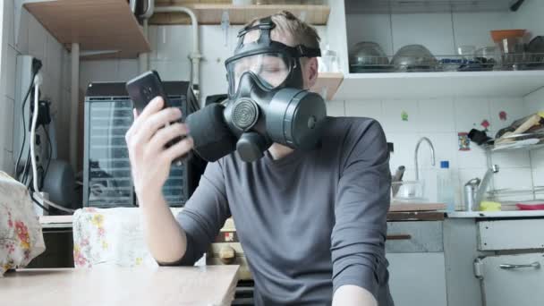 Geïrriteerde man met gasmasker spreekt smartphone in de keuken thuis. virusbescherming — Stockvideo