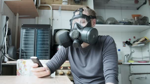 Роздратований чоловік в газовій масці говорить смартфон на кухні вдома. захист від вірусів — стокове відео