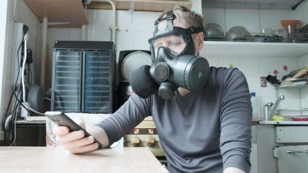 Ερεθισμένος άνθρωπος με μάσκα αερίου μιλάει smartphone στην κουζίνα στο σπίτι. προστασία από ιούς — Αρχείο Βίντεο