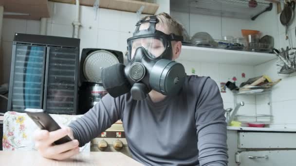 Een jongeman met een gasmasker die thuis smartphone spreekt. virusbescherming — Stockvideo