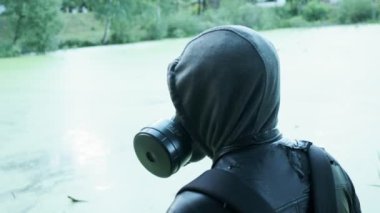 Gaz maskeli adam zehirli su deposunun yanında. Kimyasal silah koruması, virüs salgını