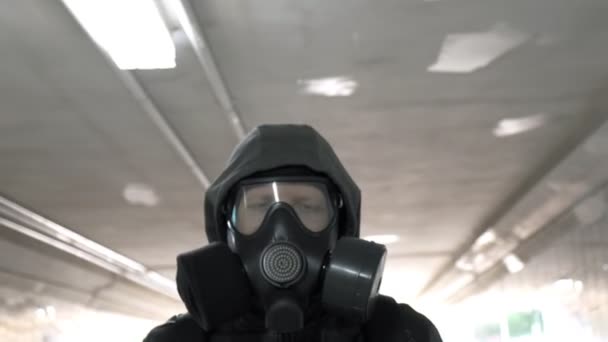 Homme en masque à gaz, veste noire avec capuche traversant un long tunnel, passage souterrain — Video