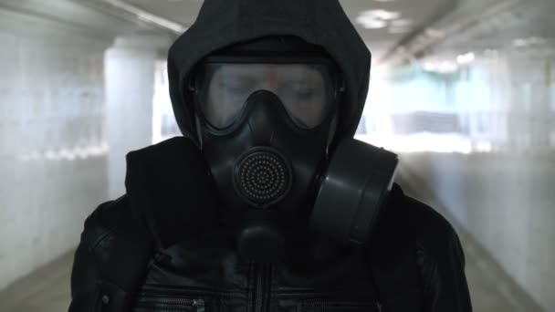 Man in gas mask, black jacket with hood walking through long tunnel, underpass — Stock Video