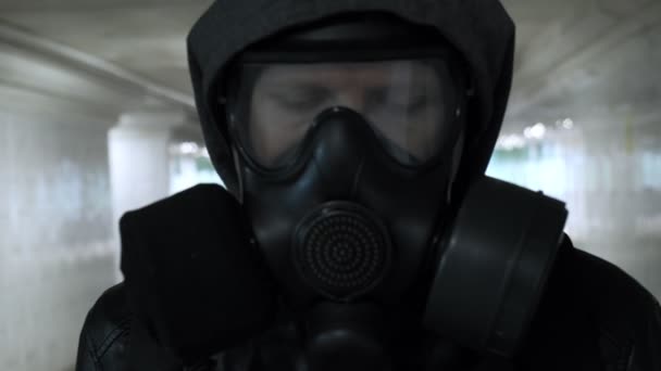 Человек в противогазе, черная куртка с капюшоном проходит через длинный туннель, подземный ход — стоковое видео