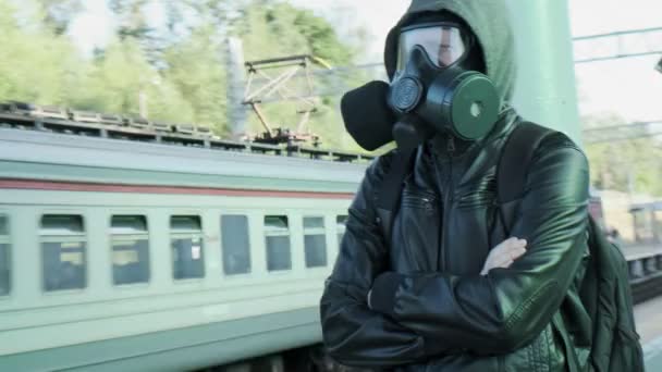 Uomo in maschera antigas con cappuccio in piedi sulla piattaforma ferroviaria di fronte al treno in movimento — Video Stock
