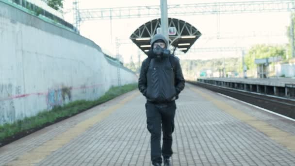 Gaz maskeli, kapüşonlu ve sırt çantalı bir adam demiryolu platformunda yürüyor. — Stok video