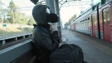 Gaz maskeli, kapüşonlu siyah ceketli garip bir adam tren istasyonunda trene biniyor.
