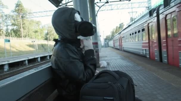 Παράξενος άνθρωπος με μάσκα αερίου, μαύρο σακάκι με κουκούλα παίρνει το τρένο στην πλατφόρμα του σιδηροδρόμου — Αρχείο Βίντεο