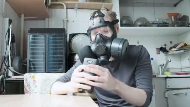 ガスマスクの男はスマートフォンを持ち家庭用キッチンで手で回転させ — ストック動画