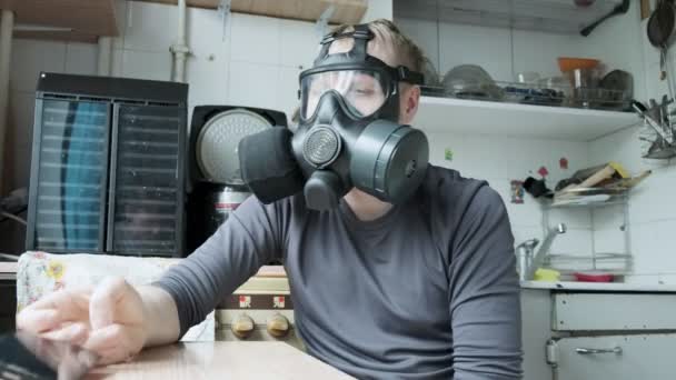 Kaukaski mężczyzna w masce gazowej bierze smartfon w ręce, śmieje się w domu kuchnia — Wideo stockowe