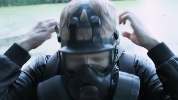 Людина кладе газову маску на обличчя, носить капюшон на голову, стоячи на відкритому повітрі біля озера — стокове відео
