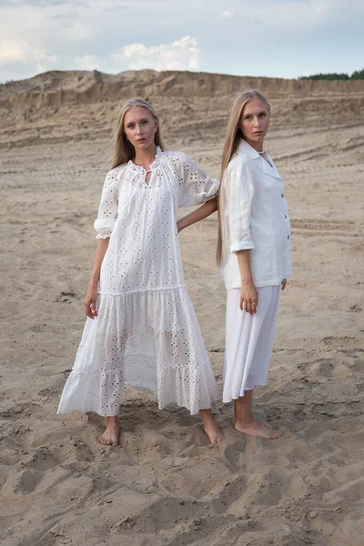 Дві молоді сестри-близнюки позують в пустелі або піщаному кар'єрі в елегантному білому одязі — стокове фото