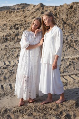 Çölde poz veren iki küçük ikiz kız kardeş ya da zarif beyaz elbiseli kum ocağı.