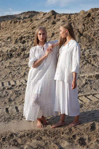 Дві привабливі молоді сестри-близнюки позують в піщаному кар'єрі в елегантному білому одязі — стокове фото