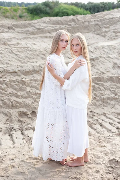 Two attractive young twin sisters posing at sand quarry in elegant white clothes — Stock Photo, Image