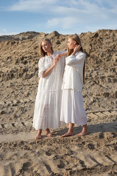Дві молоді сестри-близнюки позують в пустелі або піщаному кар'єрі в елегантному білому одязі — стокове фото