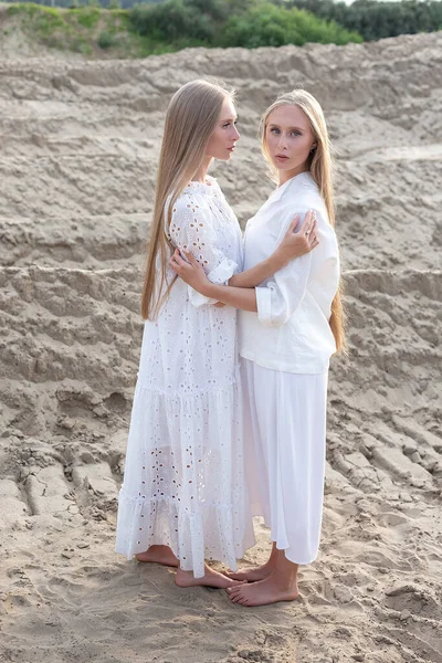 Duas jovens irmãs gêmeas atraentes posando na pedreira de areia em roupas brancas elegantes — Fotografia de Stock