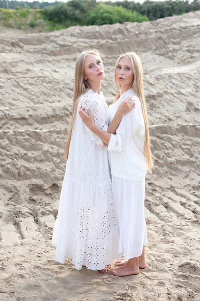 Two attractive young twin sisters posing at sand quarry in elegant white clothes — Stock Photo, Image