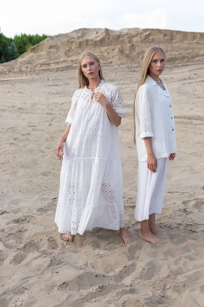 Дві привабливі молоді сестри-близнюки позують на піщаному кар'єрі в елегантному білому одязі — стокове фото