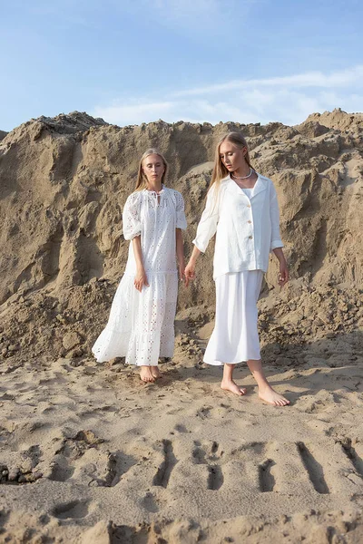 Дві привабливі молоді сестри-близнюки позують на піщаному кар'єрі в елегантному білому одязі — стокове фото