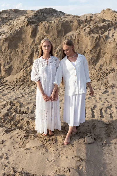 Dos hermanas gemelas jóvenes atractivas posando en la cantera de arena con ropa blanca elegante — Foto de Stock