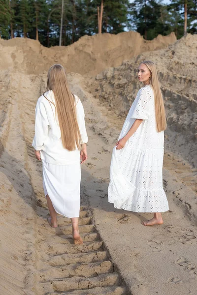 Deux belles jeunes sœurs jumelles posant à la carrière de sable dans des vêtements blancs élégants — Photo