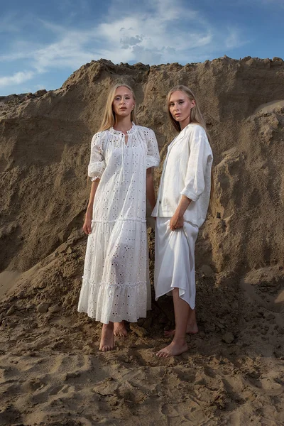 Deux belles jeunes sœurs jumelles posant à la carrière de sable dans des vêtements blancs élégants — Photo