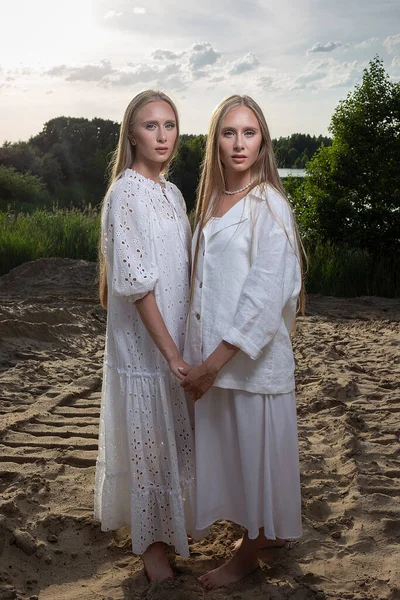 Jeunes jumeaux aux longs cheveux blonds posant sur la plage de sable en vêtements blancs élégants — Photo