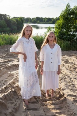 İki çekici genç kız kardeş kumsalda zarif beyaz giysiler içinde poz veriyorlar.