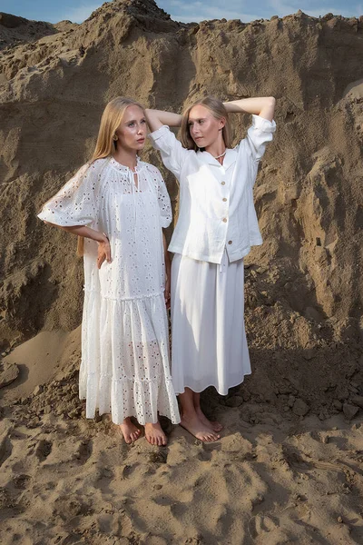 Duas jovens irmãs gêmeas atraentes posando na pedreira de areia em roupas brancas elegantes — Fotografia de Stock