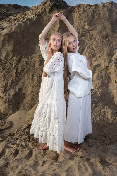 Δύο ελκυστικές δίδυμες αδελφές ποζάρουν σε λατομείο άμμου με κομψά λευκά ρούχα — Φωτογραφία Αρχείου