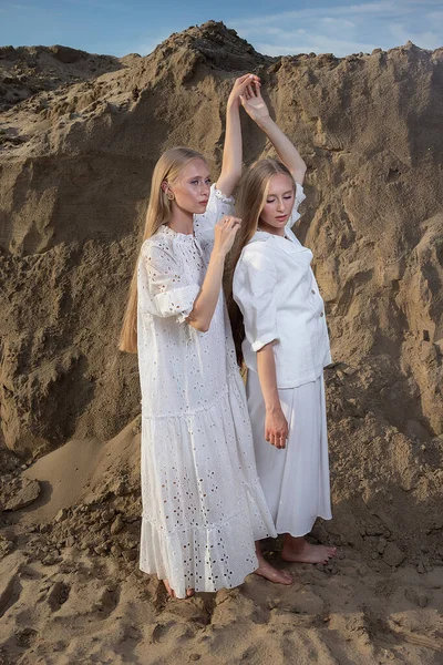 Δύο ελκυστικές δίδυμες αδελφές ποζάρουν σε λατομείο άμμου με κομψά λευκά ρούχα — Φωτογραφία Αρχείου