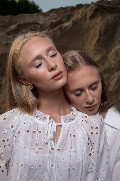Two young blond pretty twins posing at sand quarry in elegant white clothes — Stock Photo, Image