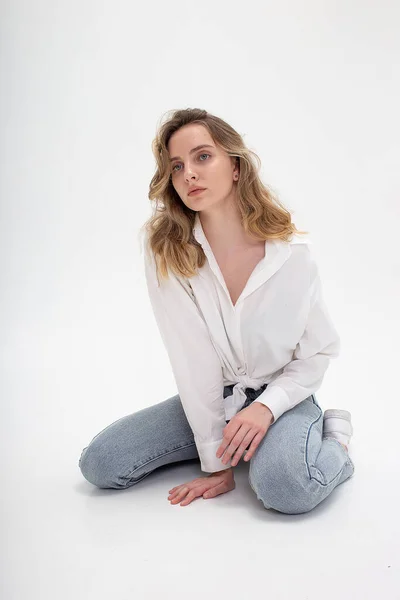 Beyaz gömlekli, mavi kotlu beyaz bir kız stüdyoda poz veriyor.