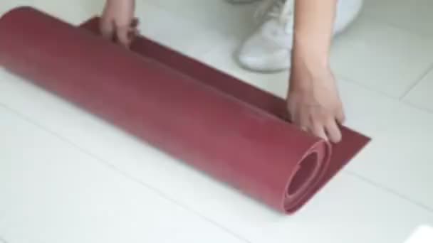 Közelkép a fiatal karcsú lány kezén a sportruházatban kibontott jóga szőnyegen a padlón — Stock videók