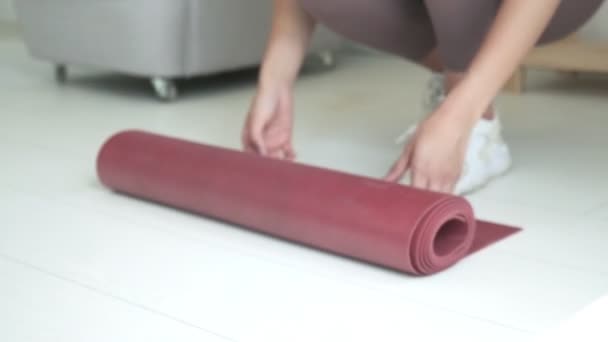 Close-up op handen van jong slank meisje in sportkleding unrolling yoga mat op de vloer — Stockvideo