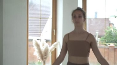 Spor kıyafetli genç bir kız atlama egzersizi yapıyor. Parlak odada ip atlıyor.