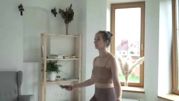 Young girl in sportswear does jump exercise in bright room with skipping rope — Stock Video