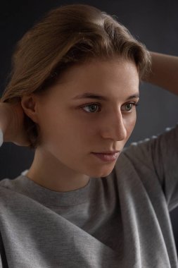 Kısa saçlı kadın siyah stüdyo arka planında gri tişörtlü poz veriyor.