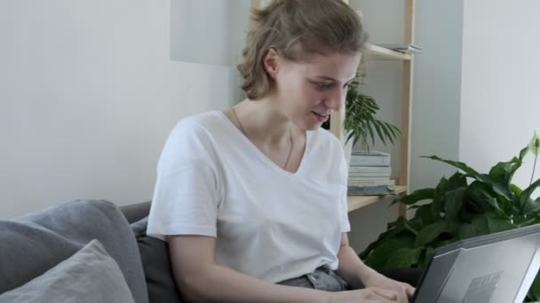 Glimlachende jonge vrouw zitten op de bank, met behulp van laptop notebook, typen bericht — Stockvideo