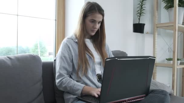 Uśmiechnięta młoda kobieta siedząca na kanapie, używająca notebooka, wpisująca wiadomość — Wideo stockowe