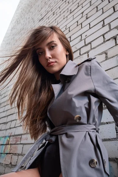 Trençkotlu çekici Asyalı model, alt noktadan duvarın yanında duruyor.