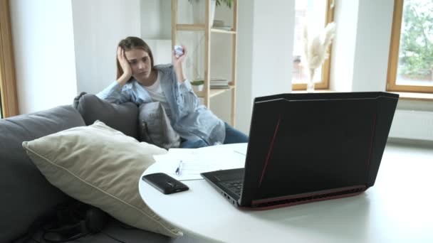 Meisje moe van haar werk zit op de bank, gooit verfrommeld papier in laptops scherm — Stockvideo