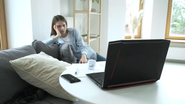 Meisje moe van haar werk zit op de bank, gooit verfrommeld papier in laptops scherm — Stockvideo