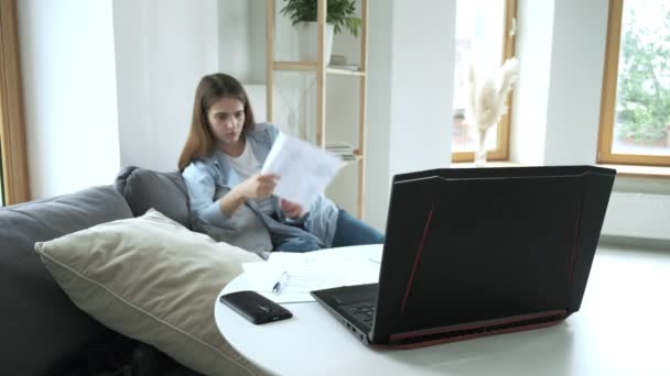 Κορίτσι κουρασμένο από τη δουλειά της κάθεται στον καναπέ, ρίχνει τσαλακωμένο χαρτί στην οθόνη φορητούς υπολογιστές — Αρχείο Βίντεο